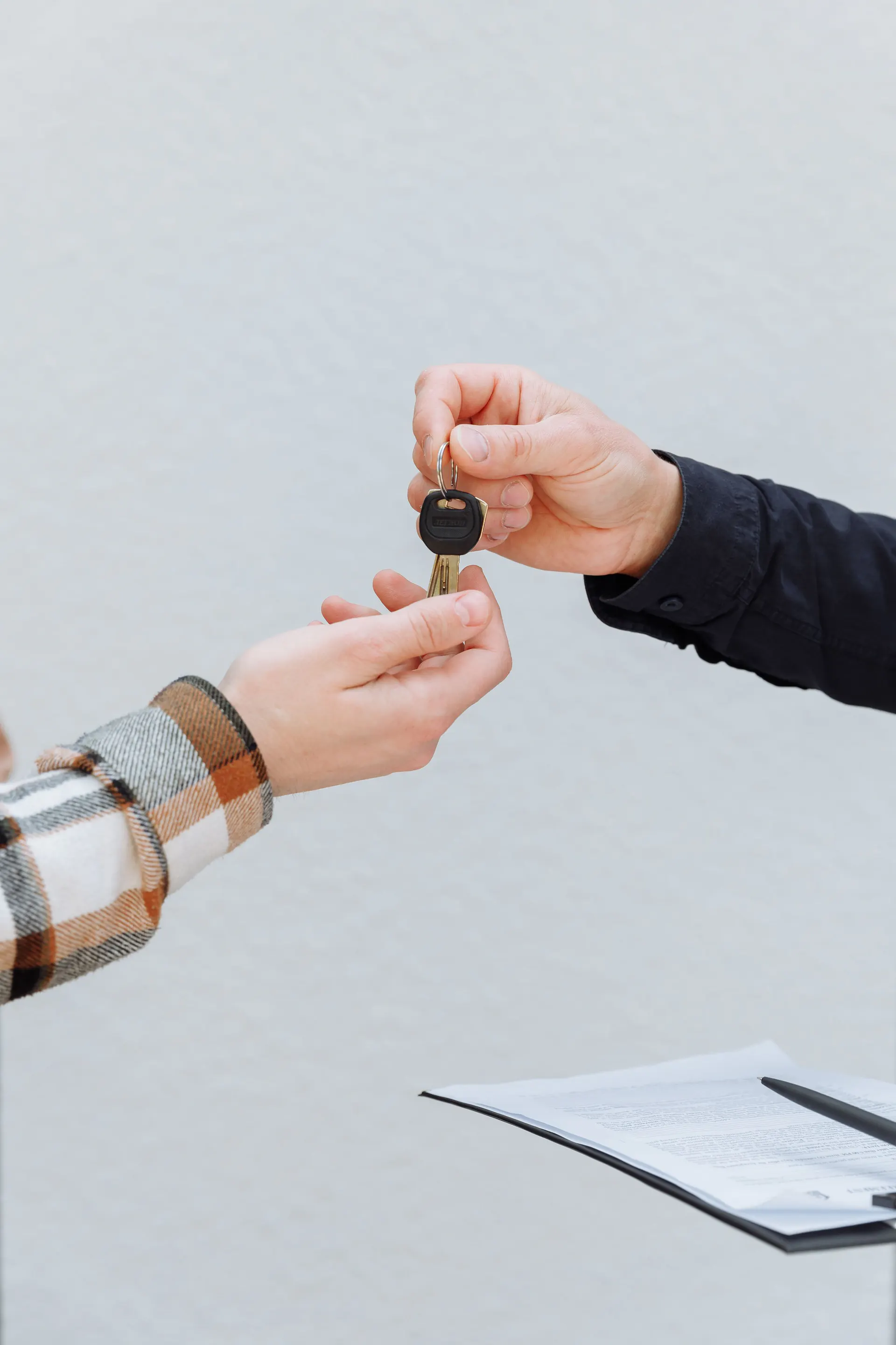 One person hands a key to another, with paperwork on a clipboard nearby.
