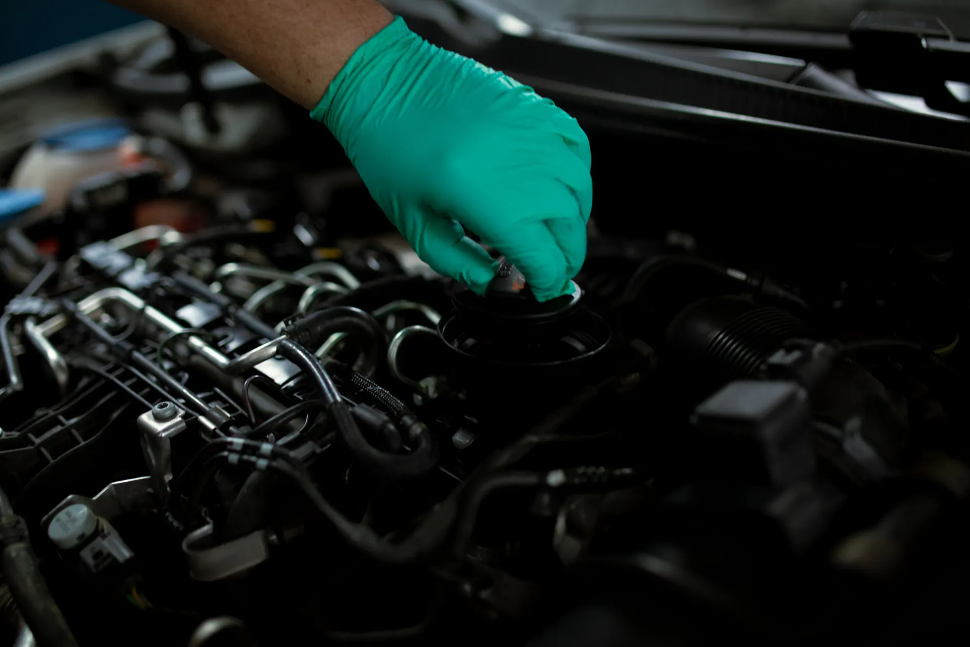 A gloved hand opens the oil filler cap on a car engine.